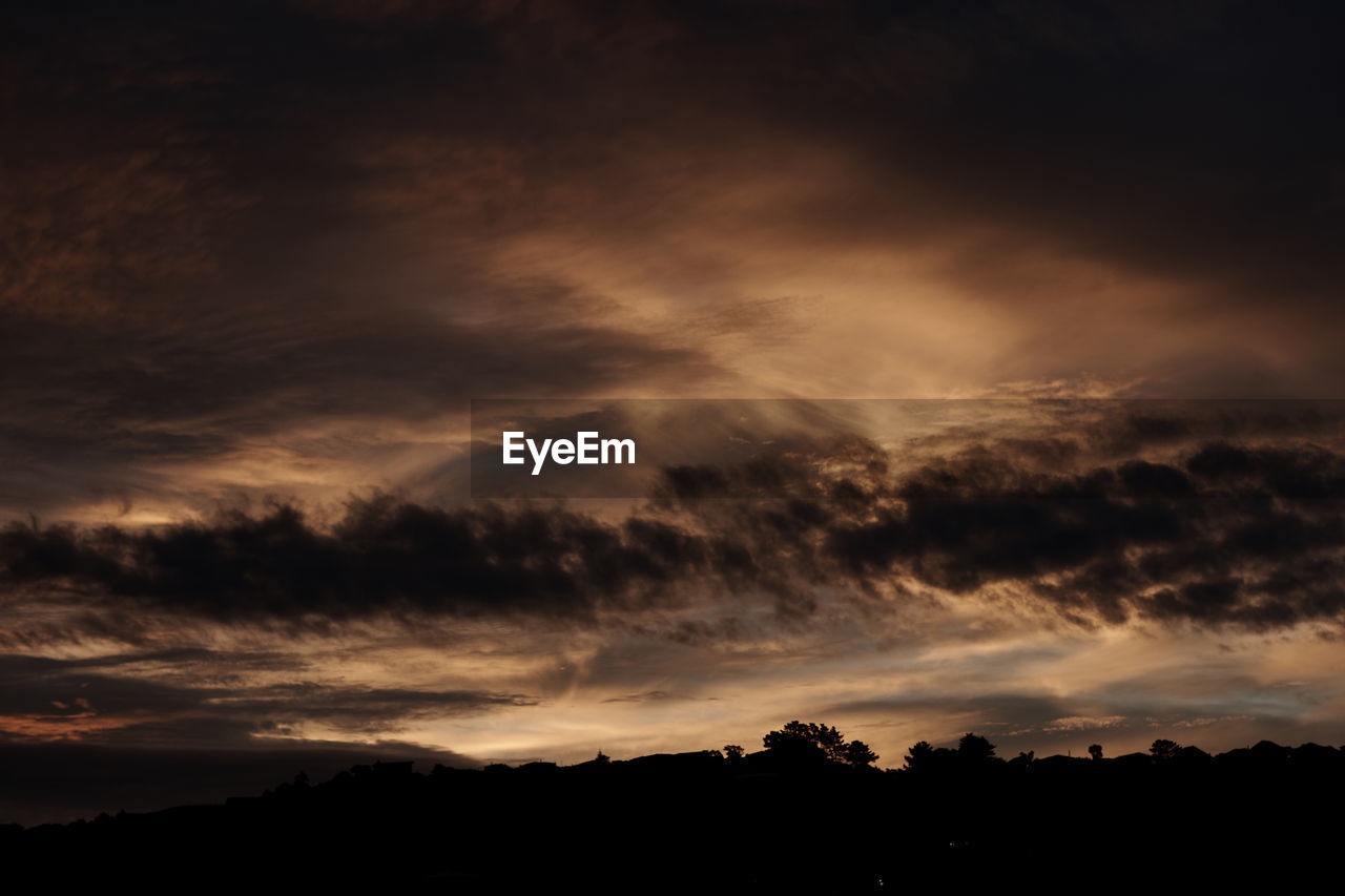 Low angle view of silhouette trees against dramatic sky