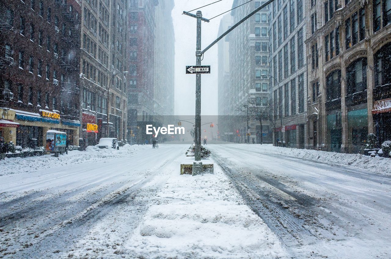 Street covered with snow amidst buildings in city during snowfall