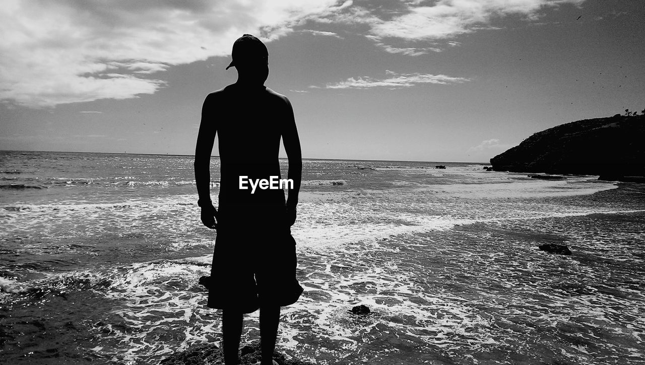 Rear view of silhouette man standing at beach against sky