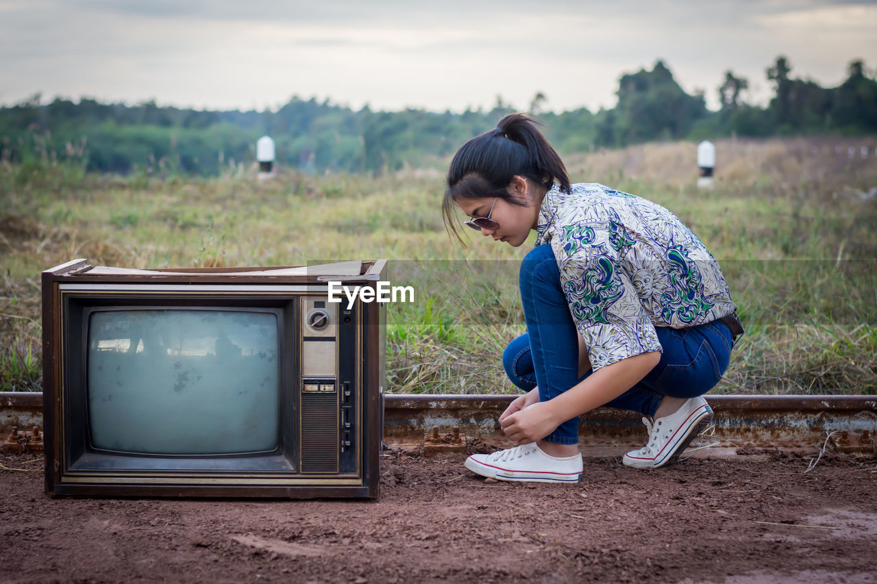 Woman wearing shoe by old television set on field