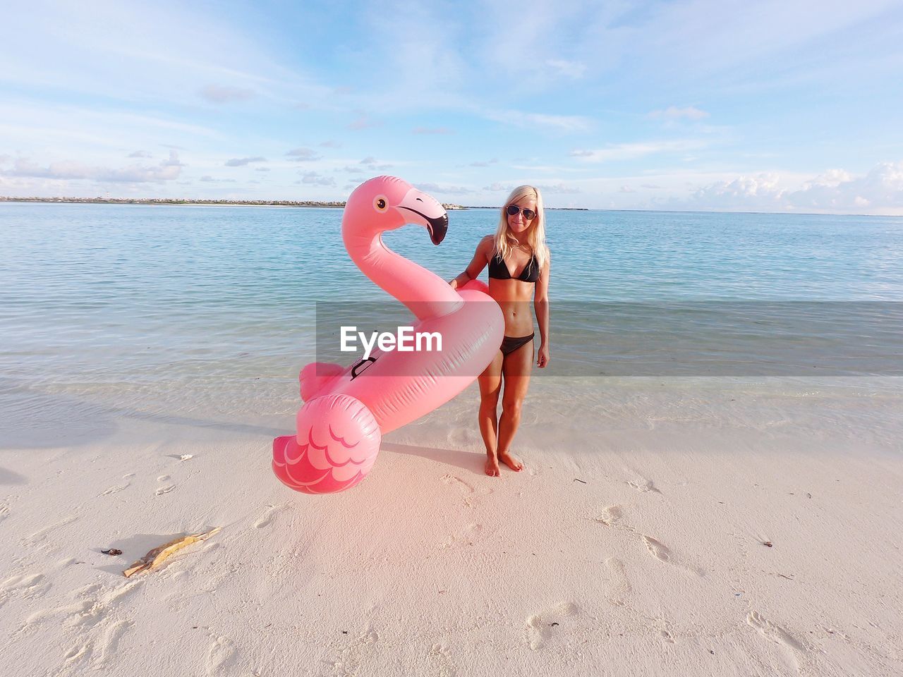 Full length of woman holding inflatable ring while standing on shore at beach