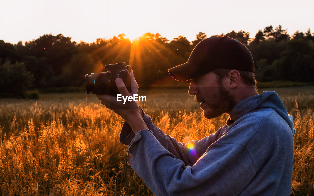 Side view of man photographing while standing on field