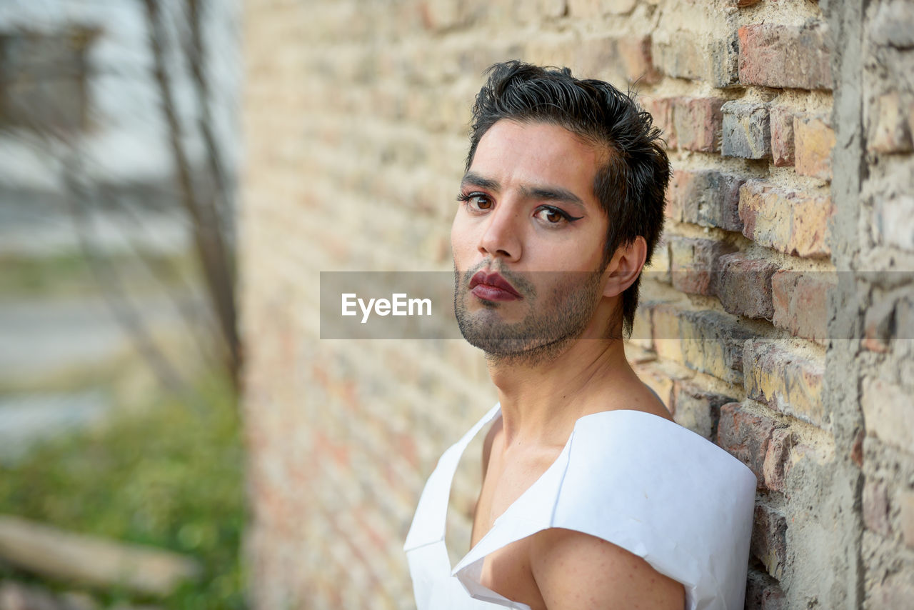 Portrait of man with make-up standing against wall