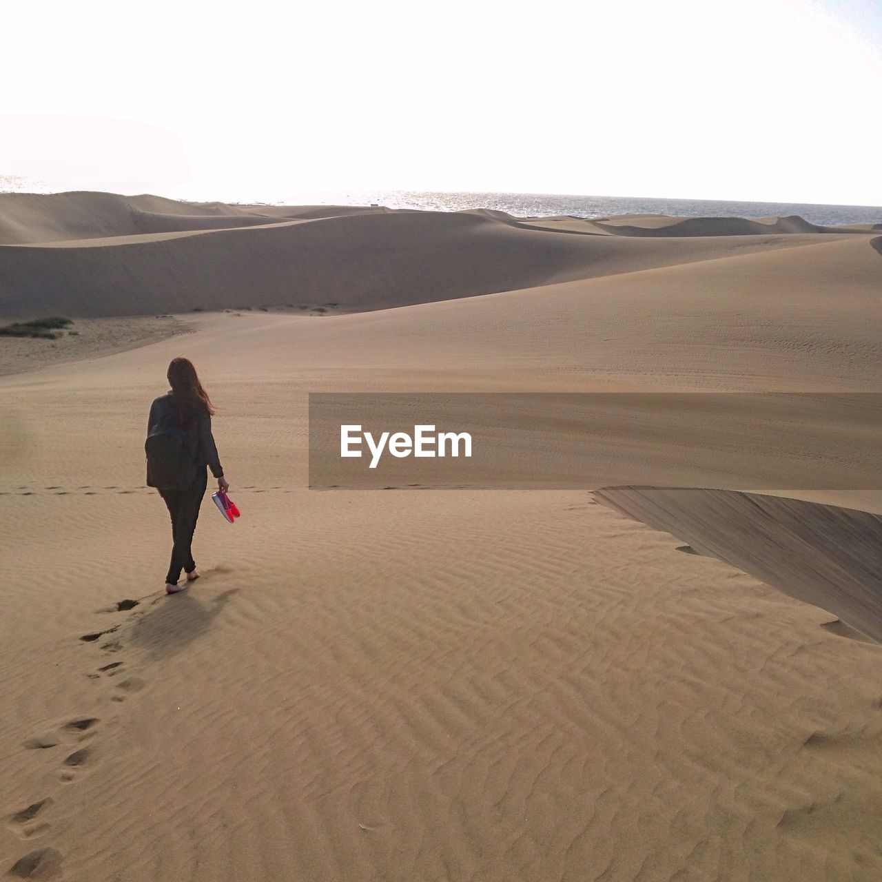 REAR VIEW OF PERSON WALKING ON SAND DUNE