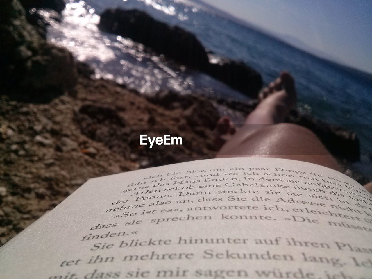 Cropped image of novel with woman leg at beach against sky