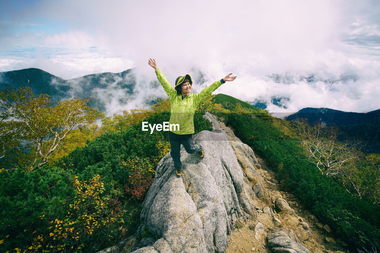 Woman with arms raised standing on mountains against sky