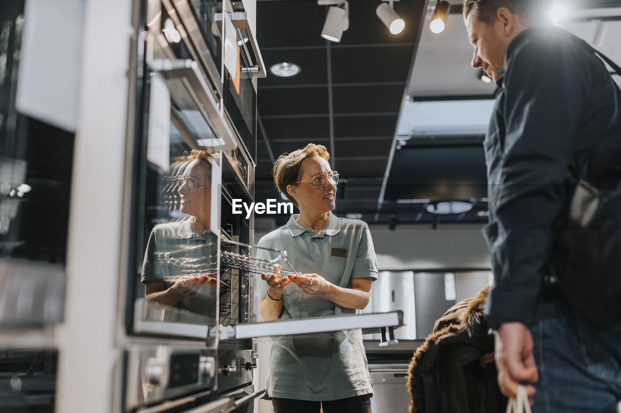 Customer looking at microwave oven while saleswoman assisting in electronics store