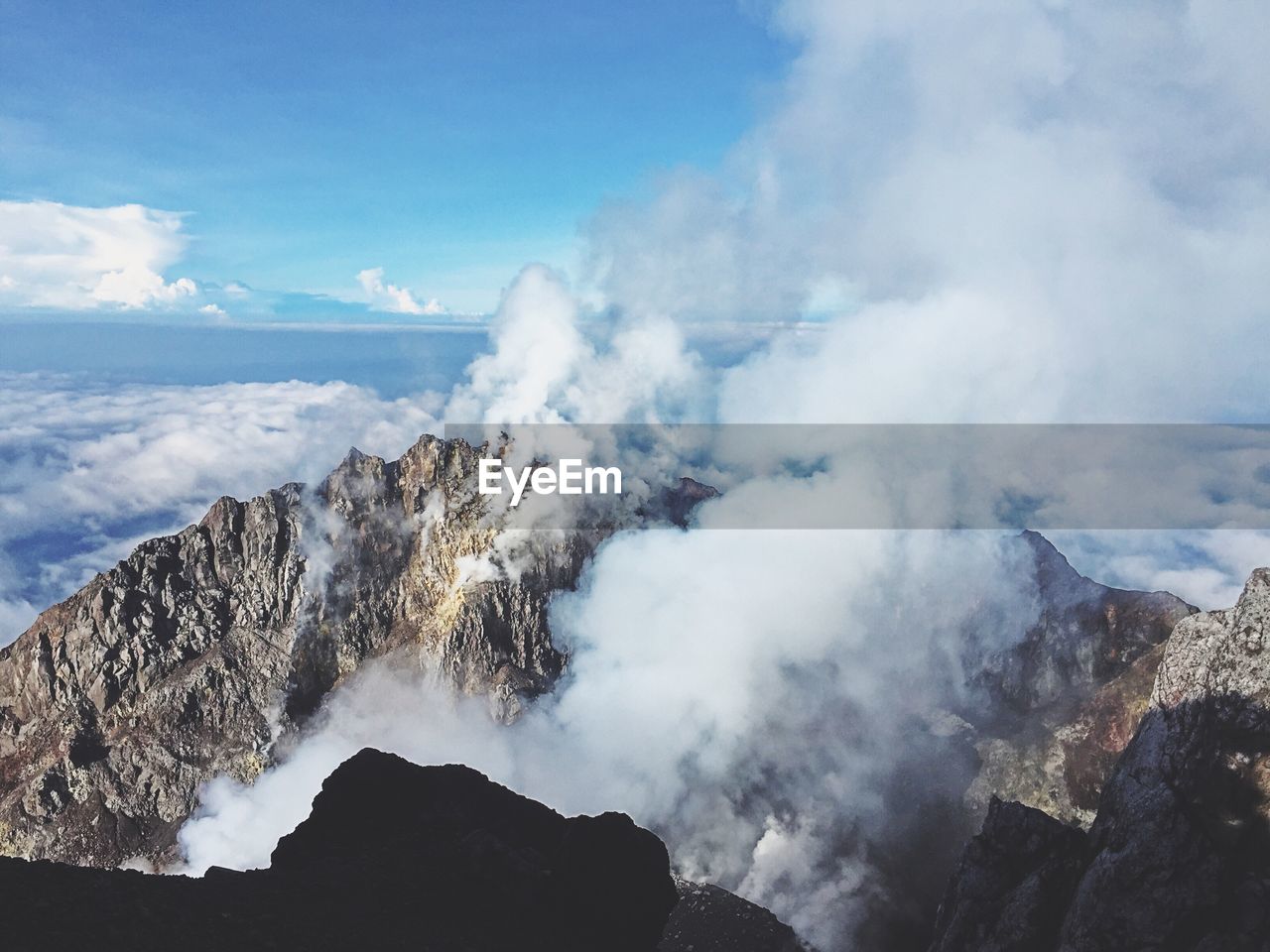High angle view of smoke emitting from mountain against sea and cloudy sky