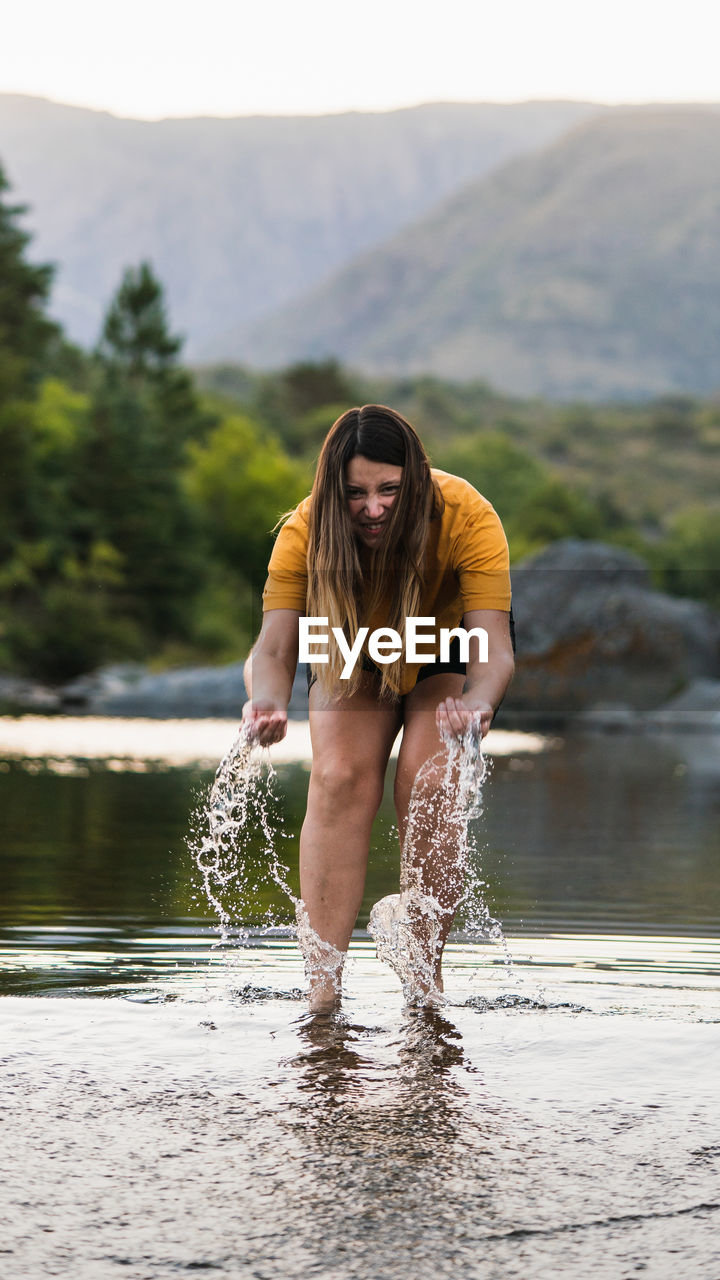 Full length portrait of woman splashing water while standing in lake