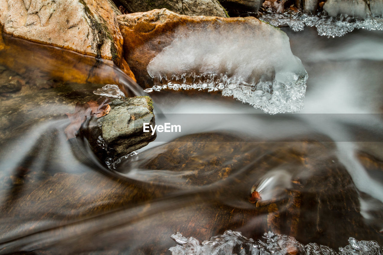 Close-up of water flowing through rocks with ice
