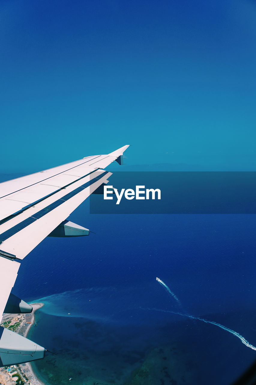 AERIAL VIEW OF SEA AND AIRPLANE AGAINST BLUE SKY