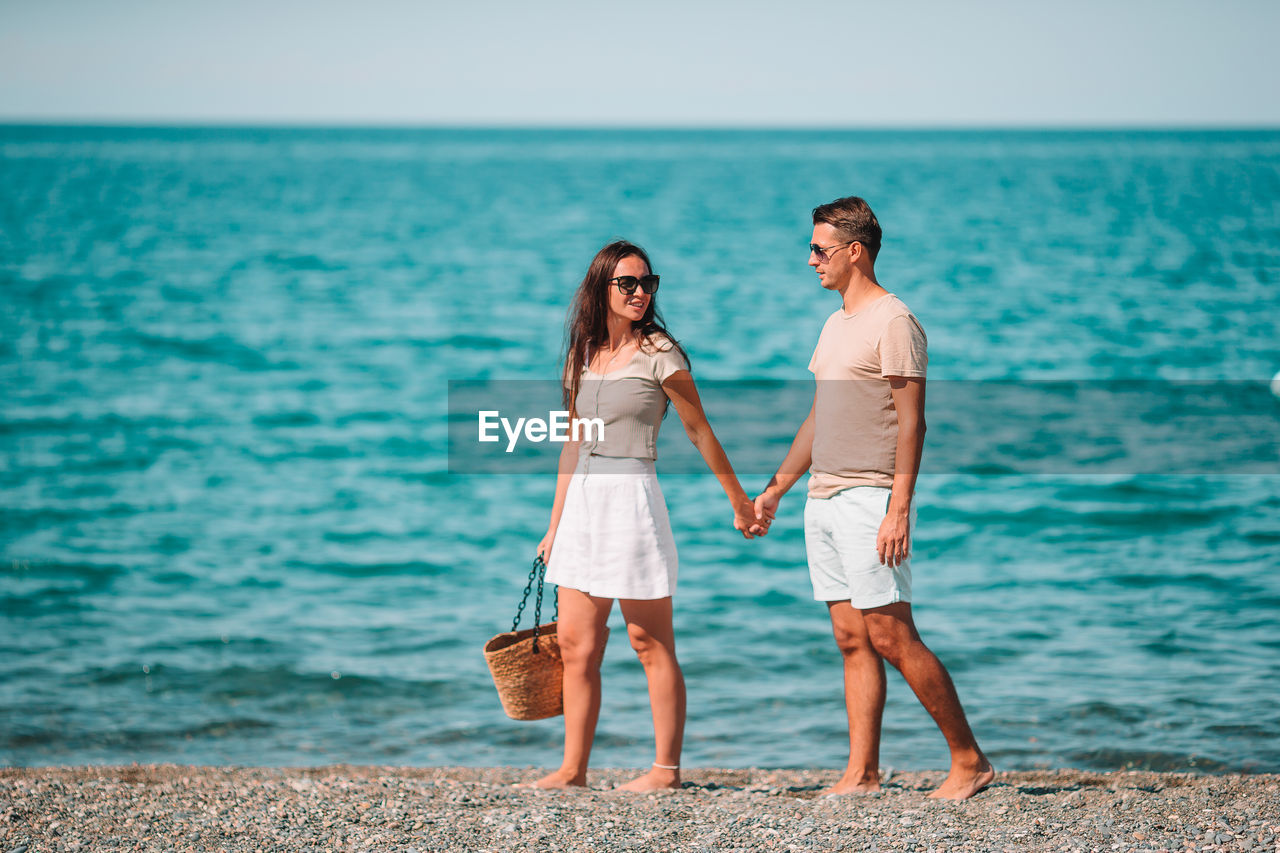 Couple holding hands standing against beach