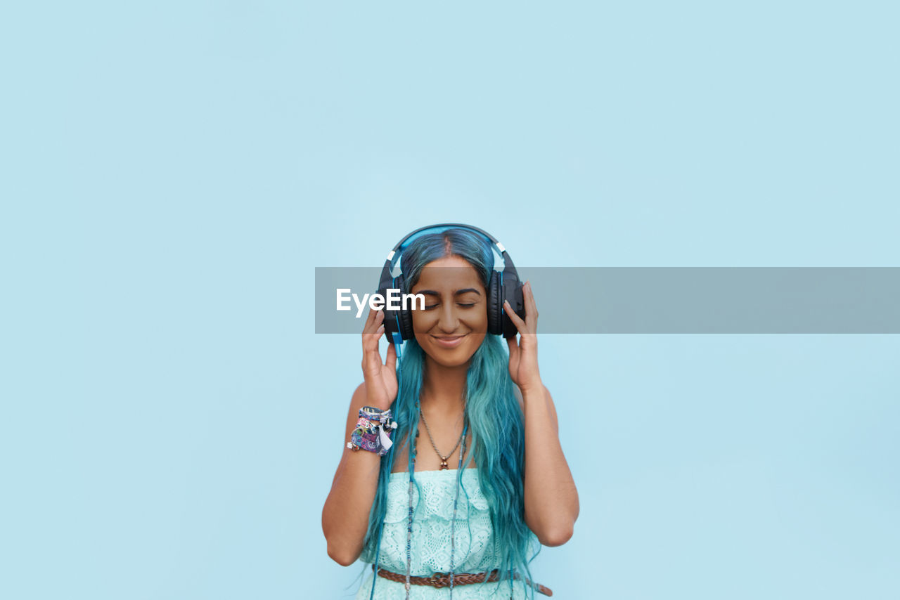 Young woman listening music against blue background