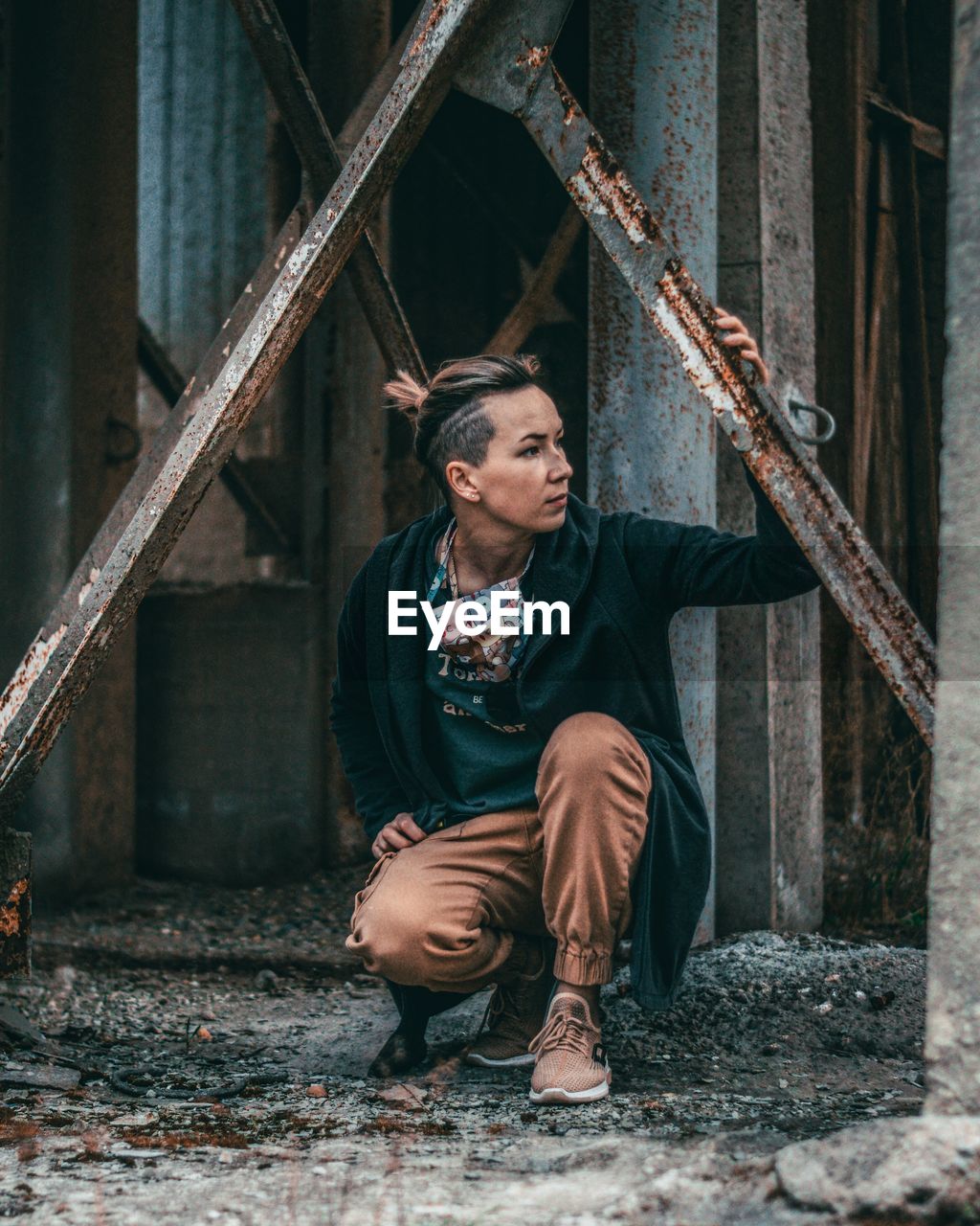 Man looking away while crouching by rusty metallic structure
