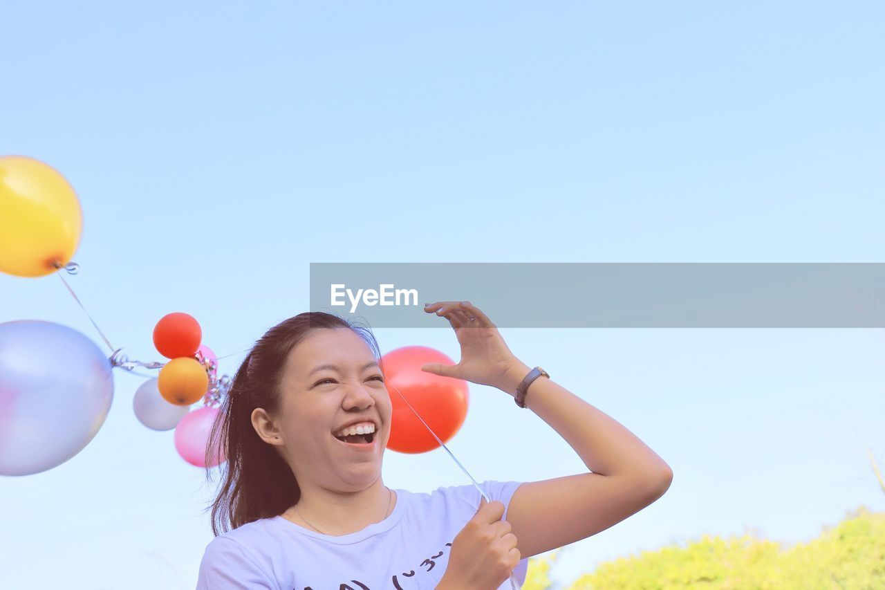 PORTRAIT OF HAPPY GIRL WITH BALLOONS IN AGAINST SKY