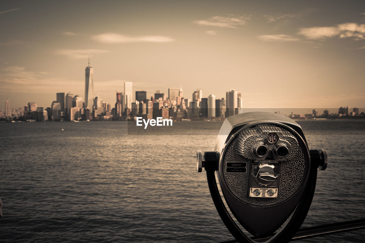 Close-up of coin-operated binoculars by river against cityscape