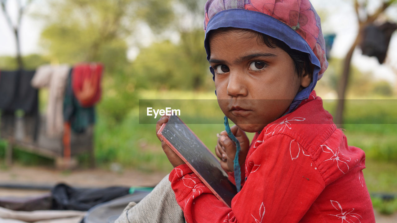 Cute little indian girl writing 123 on black school slate board, isolated over garden background.