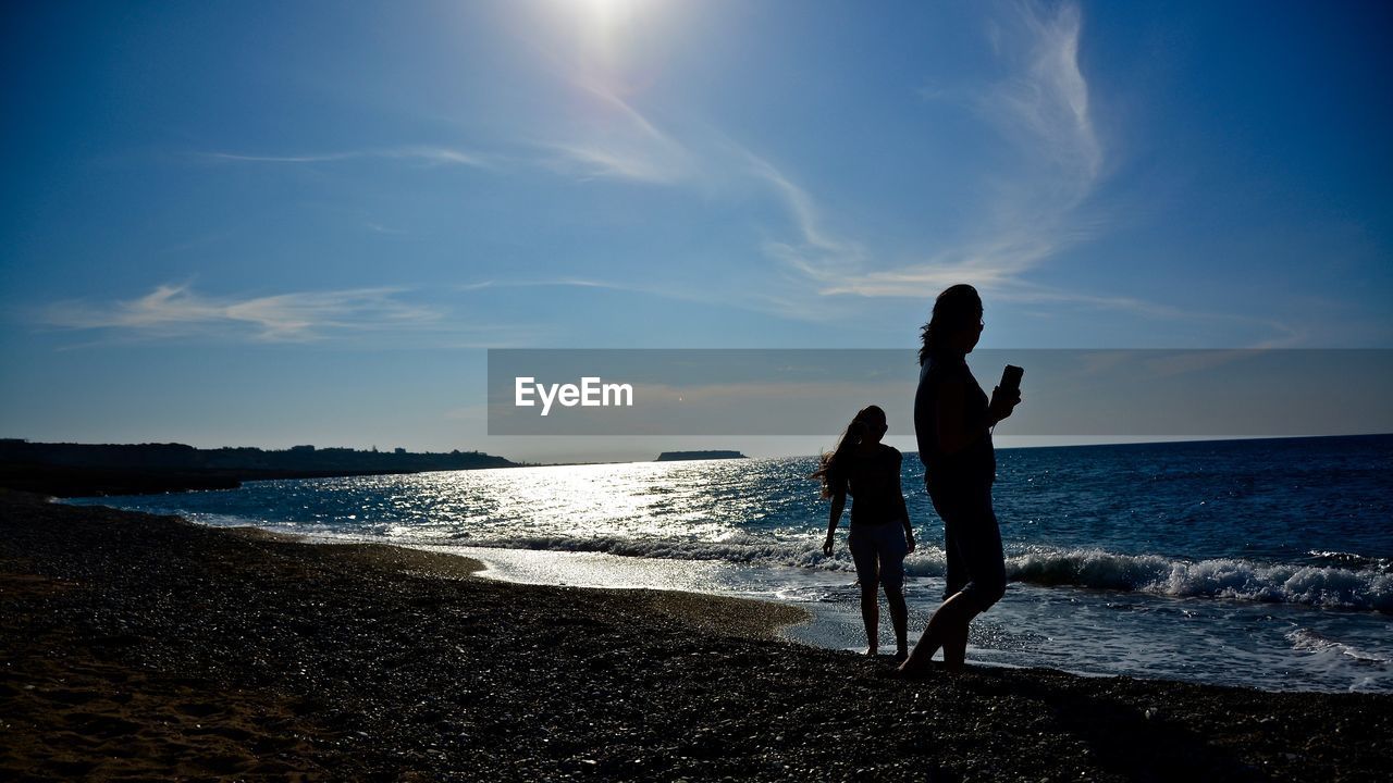 Silhouette people on shore at beach against sky