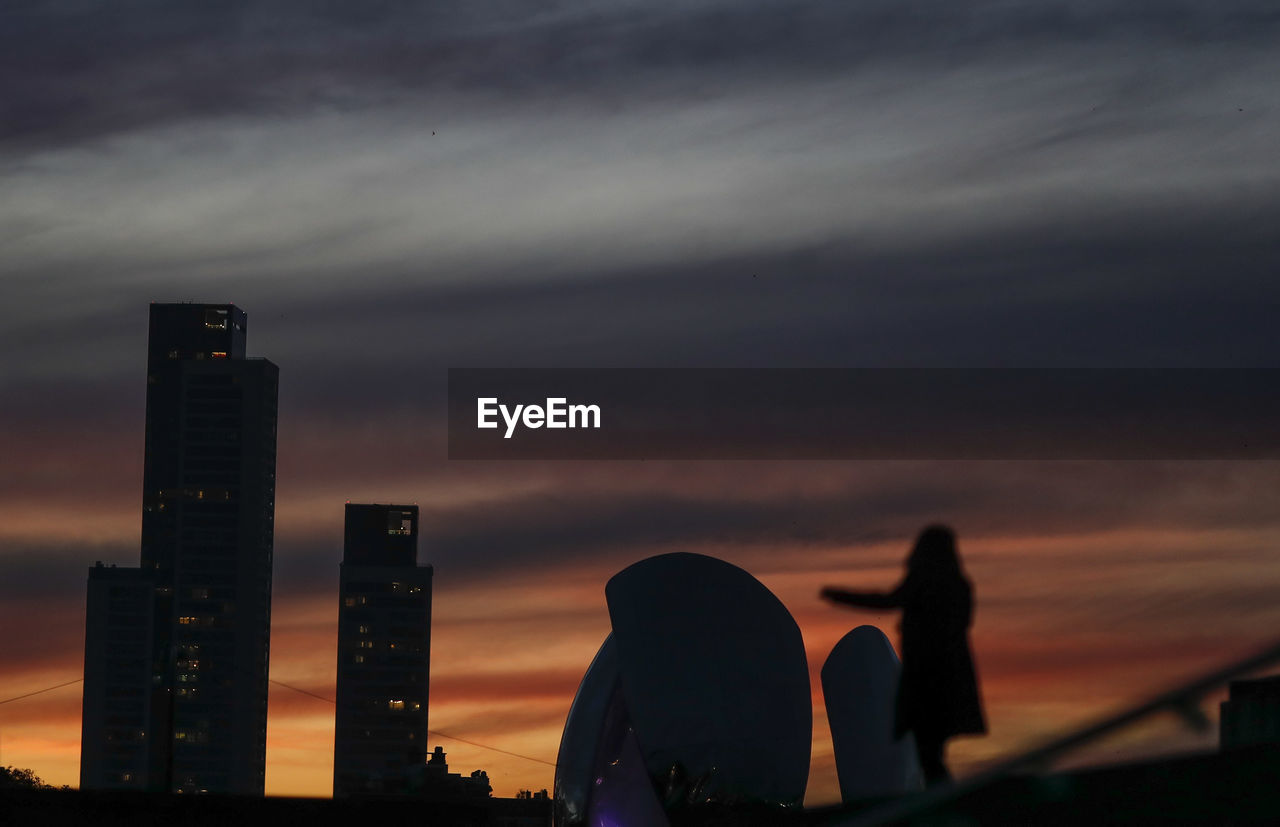 SILHOUETTE OF MODERN BUILDINGS AGAINST SKY AT SUNSET