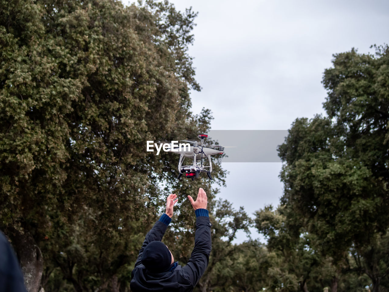 Rear view of man flying quadcopter against sky