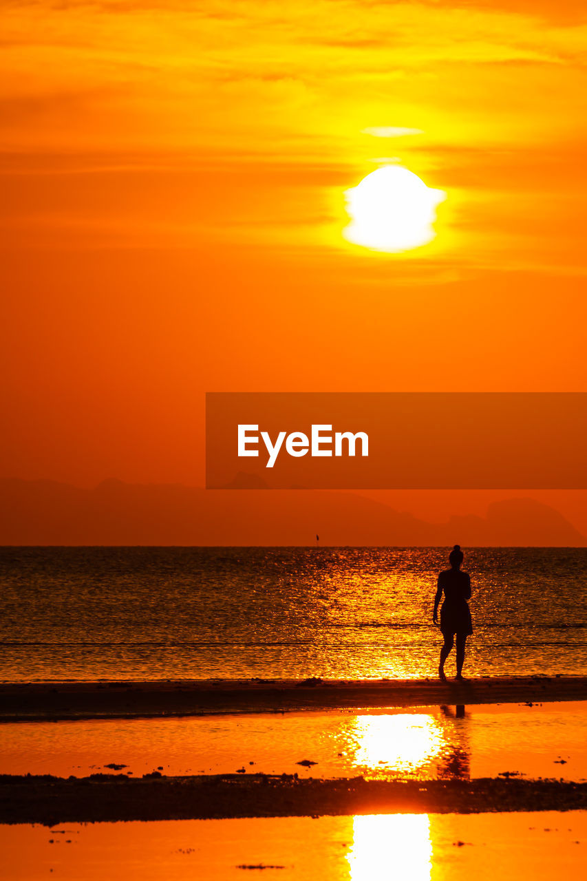 SILHOUETTE PEOPLE STANDING AT BEACH AGAINST ORANGE SKY