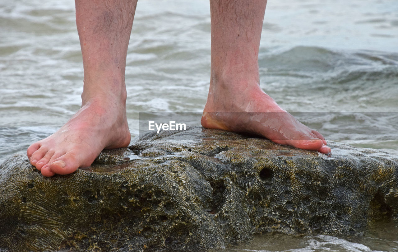 Low section of man standing on rock amidst river