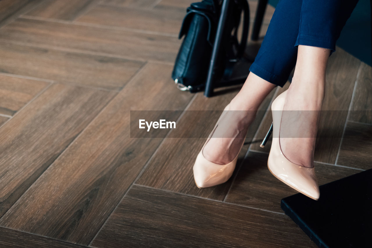 Low section of woman wearing high heels on hardwood floor