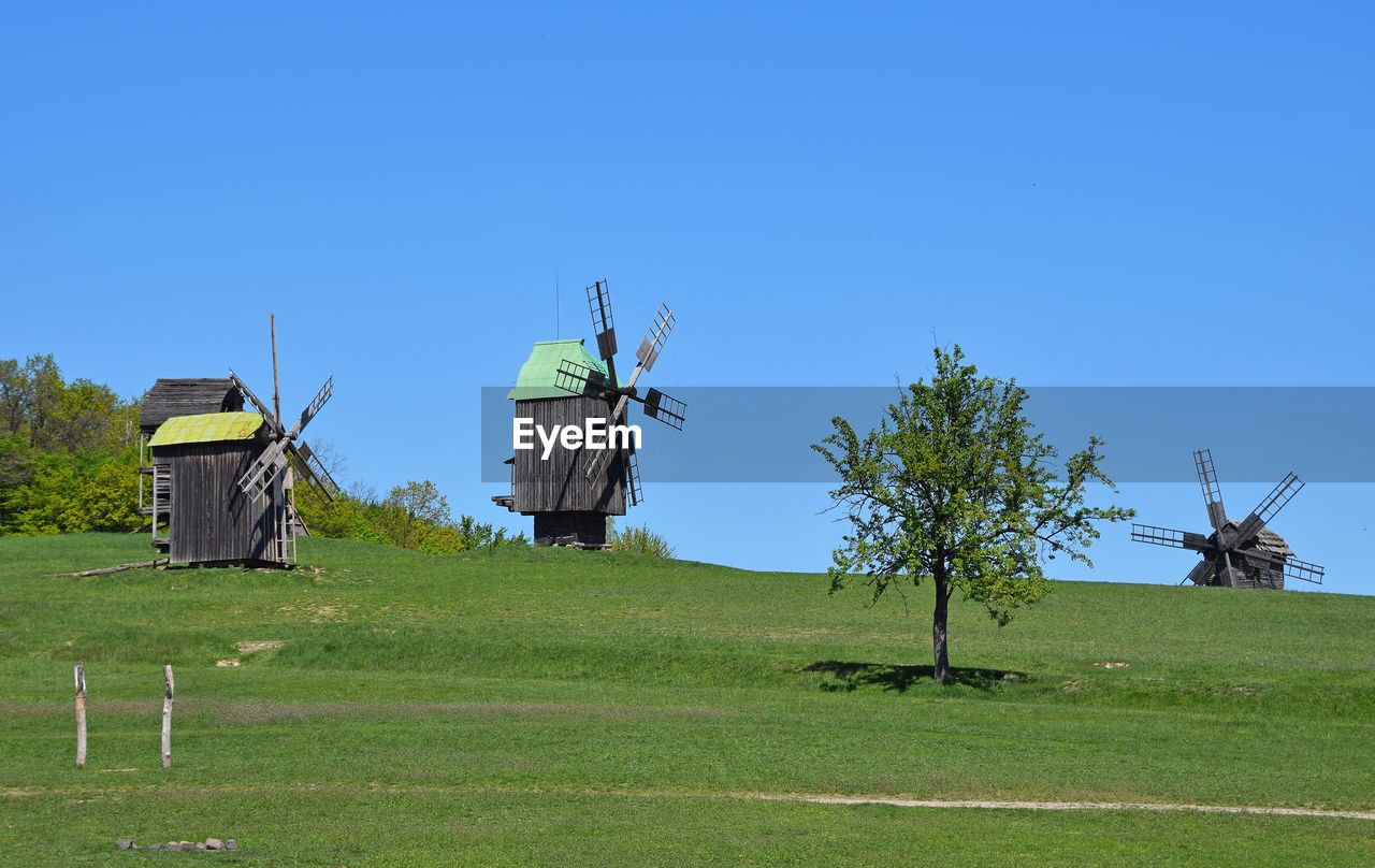 Windmills on landscape against clear blue sky