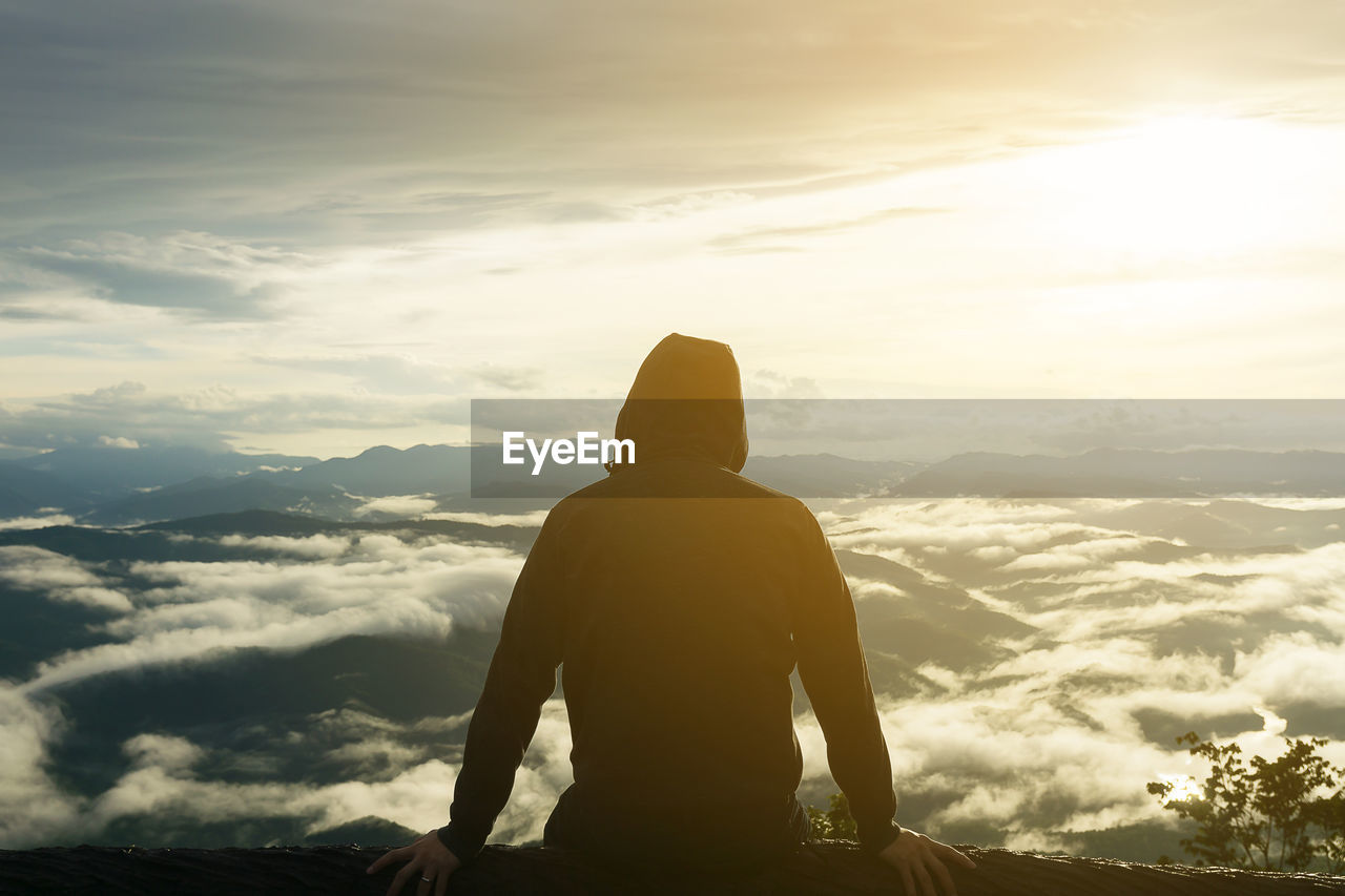 Rear view of man looking at mountain against sky during sunset