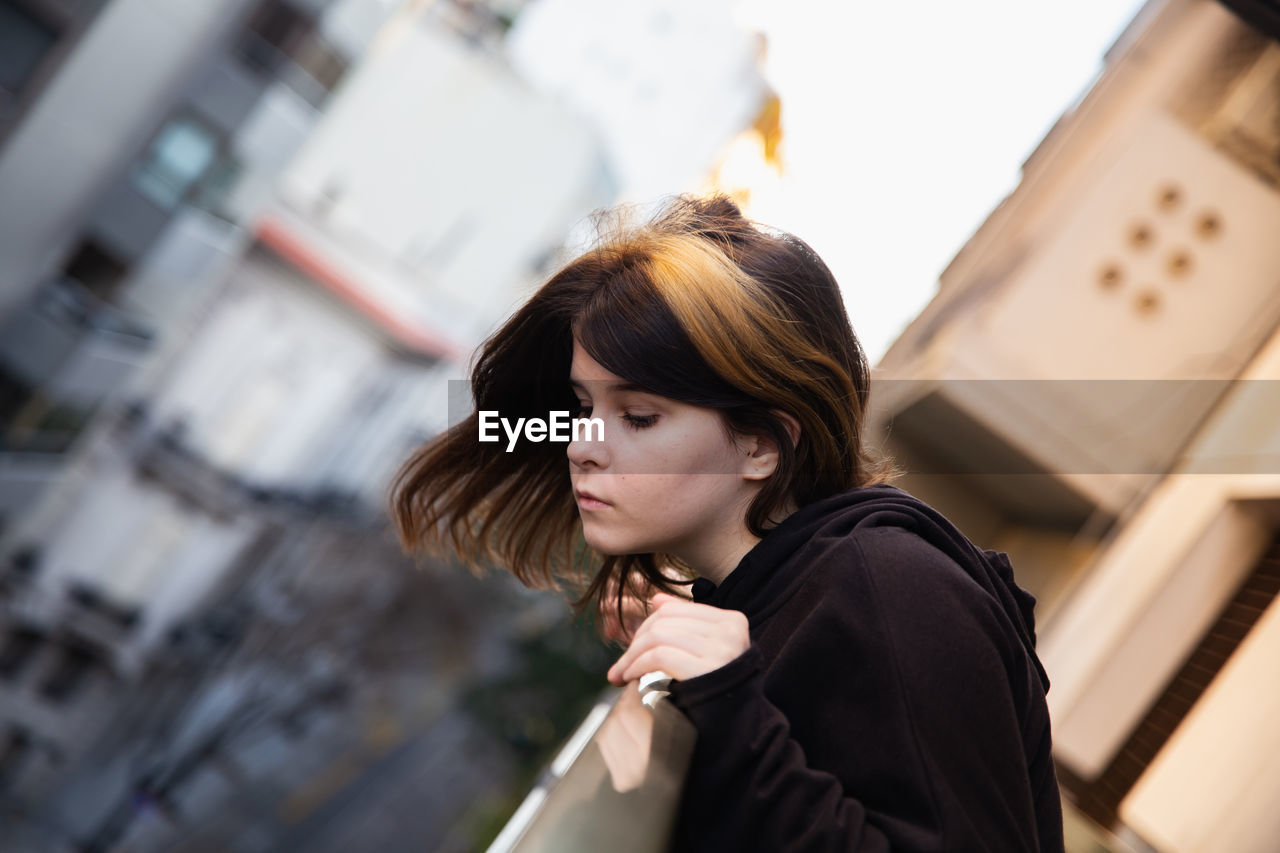 Cute teen girl looks down from the balcony of a city building