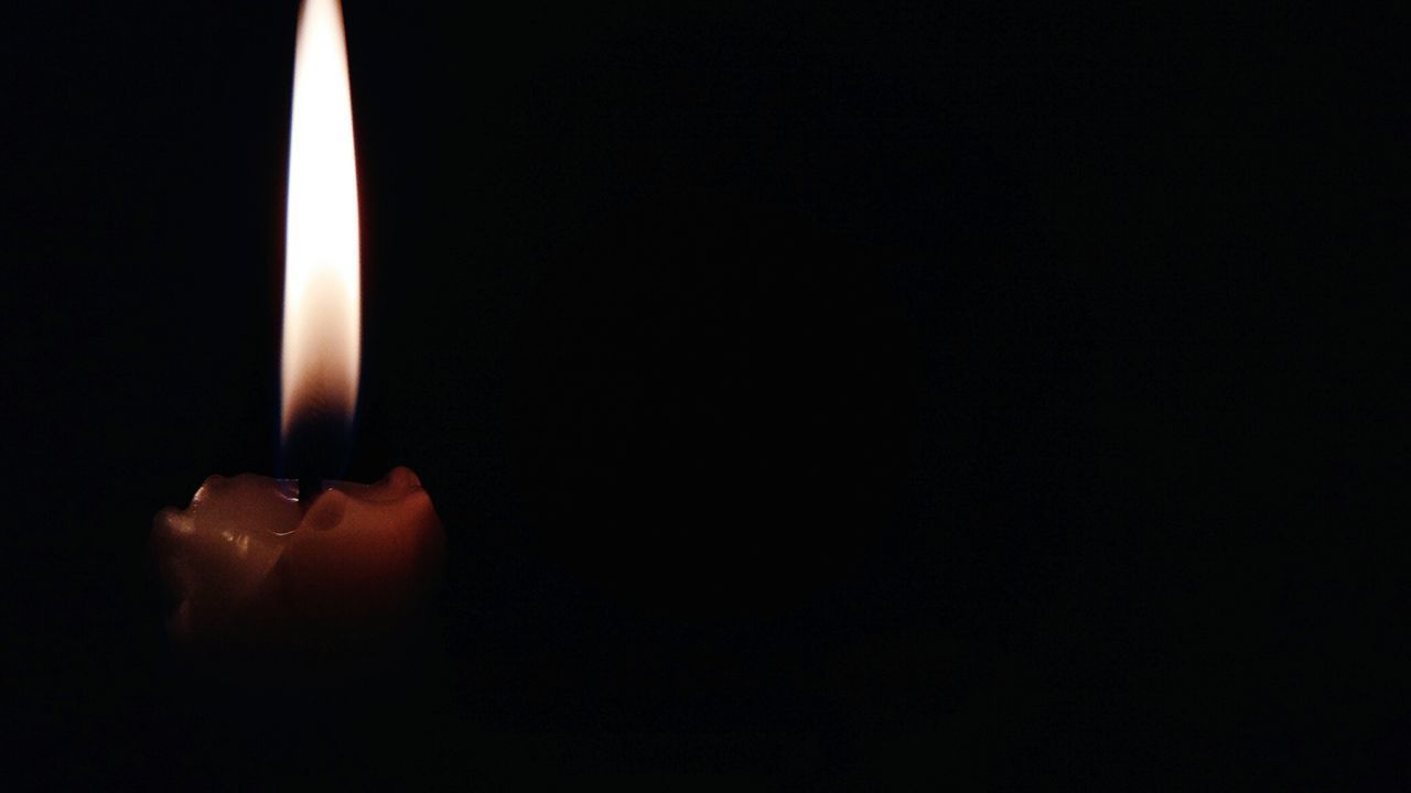 CLOSE-UP OF LIT CANDLE IN DARK ROOM