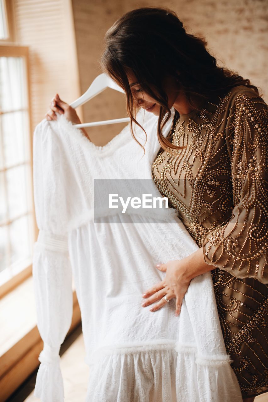 Woman holding wedding dress while standing against wall