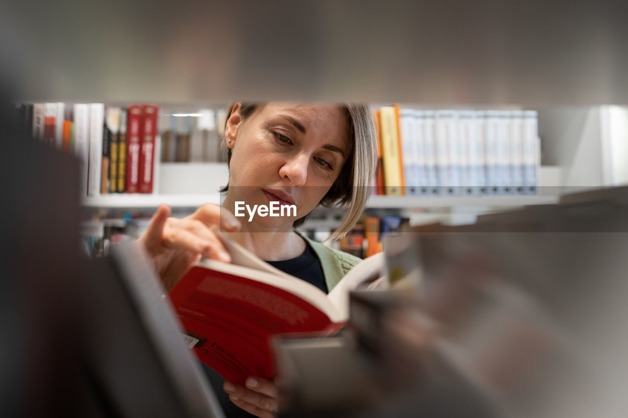 Scandinavian middle-aged woman choosing textbook, looking for literature while preparing for exam