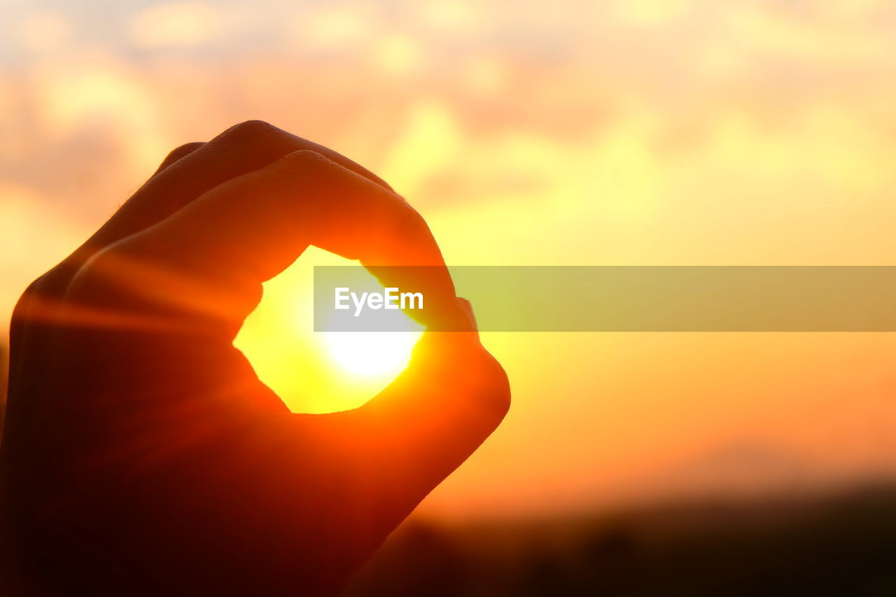 Cropped hand against sky during sunset