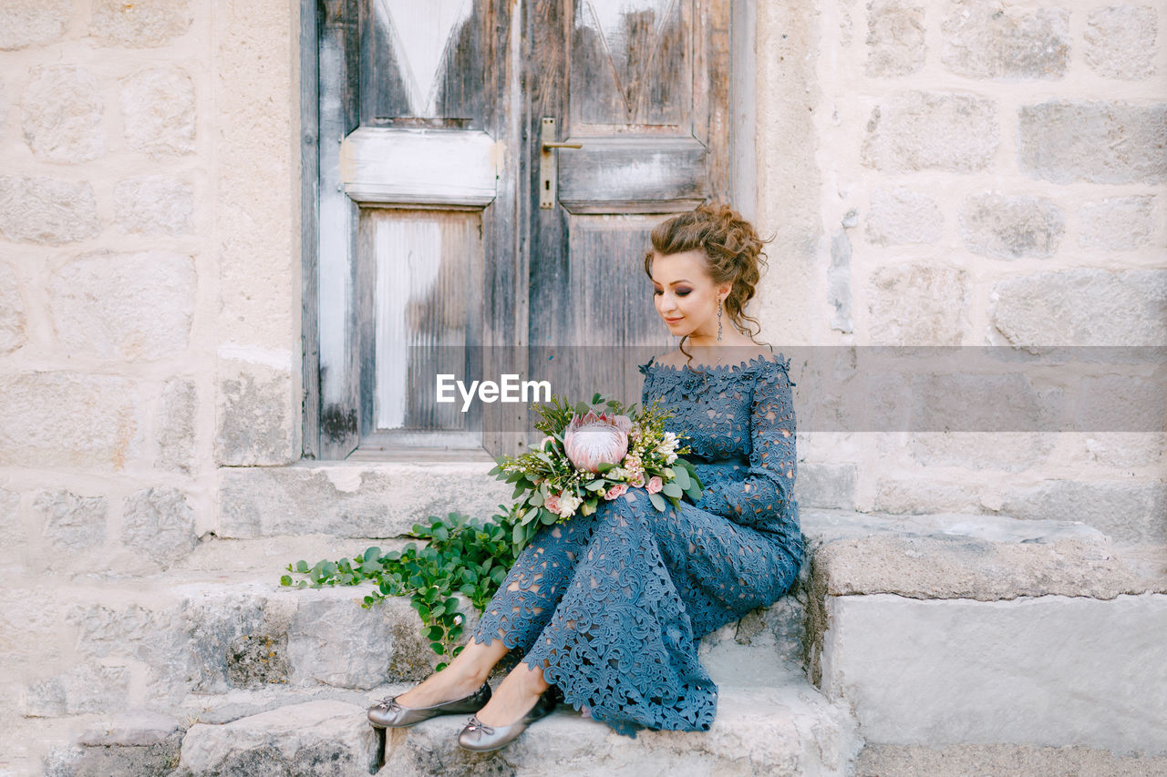 WOMAN LOOKING AT FLOWER POT AGAINST WALL