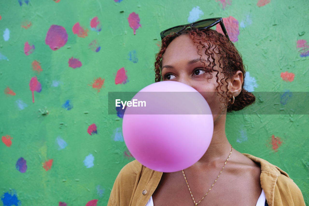 Young woman blowing bubble gum in front of wall