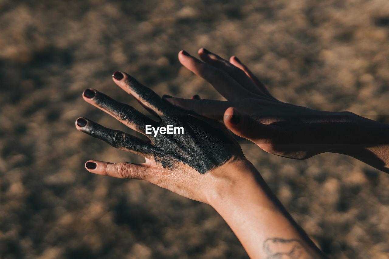 Female hands with dark mud rubbed onto them and black fingernails to show a connection to earth. 