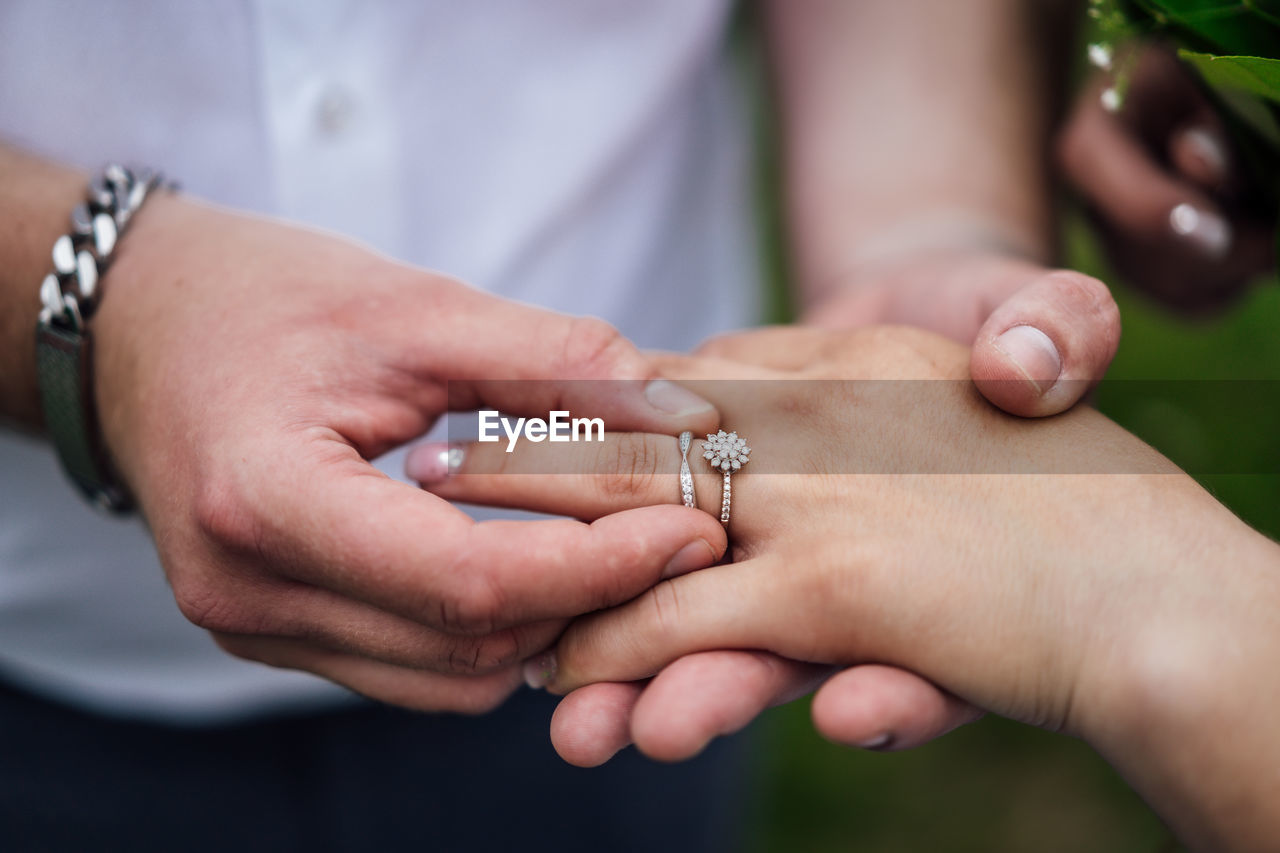 Midsection of man putting ring in woman finger outdoors