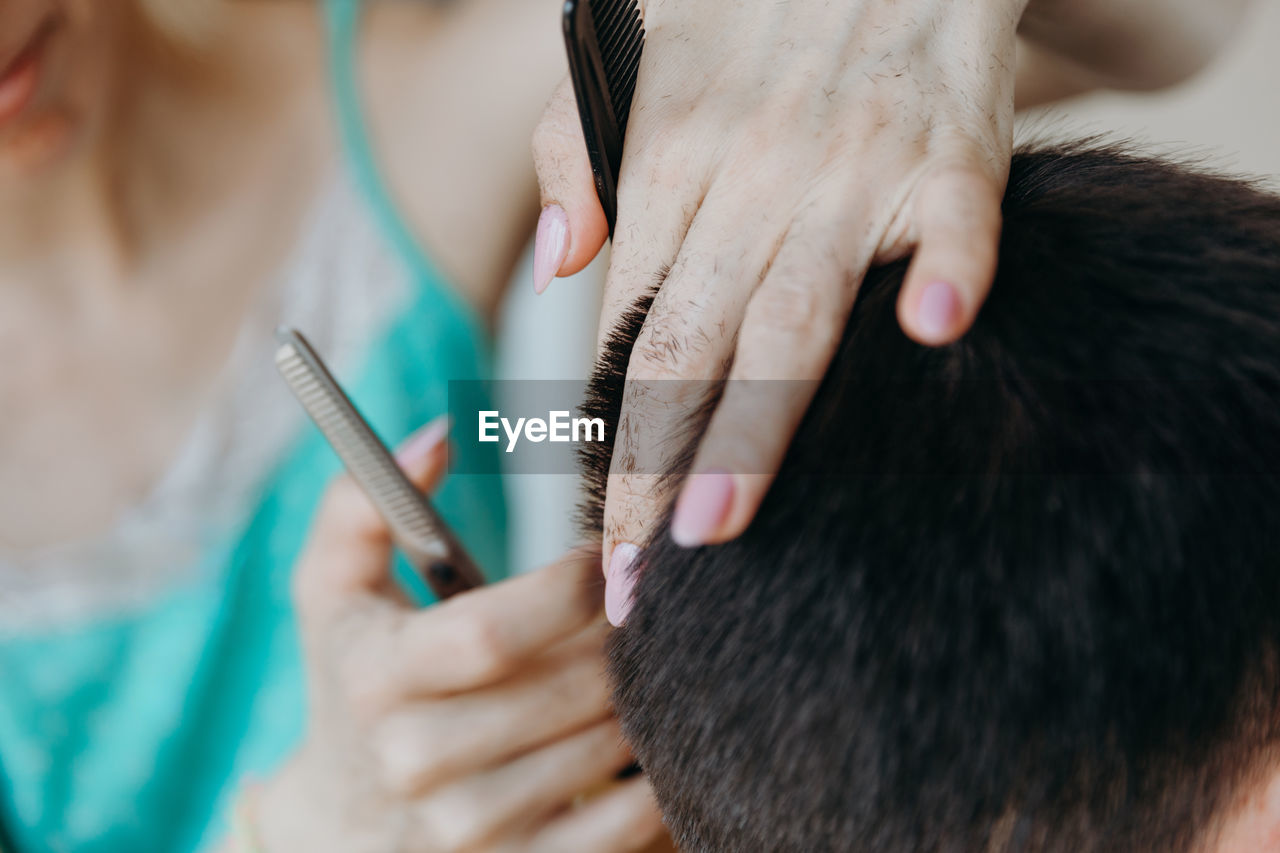 Woman hairdresser cuts hair for male client at home.