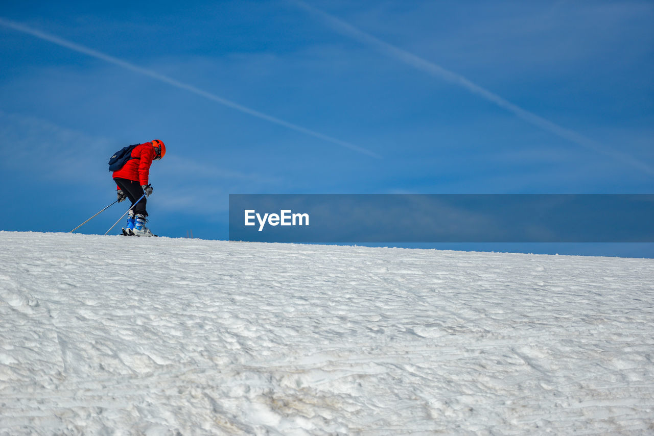 Man skking on snowcapped mountain against blue sky