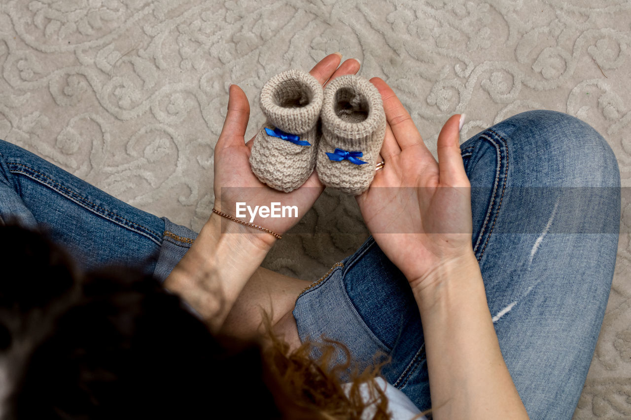 Pregnant woman holds baby booties in her hands while sitting on the sofa. close-up.
