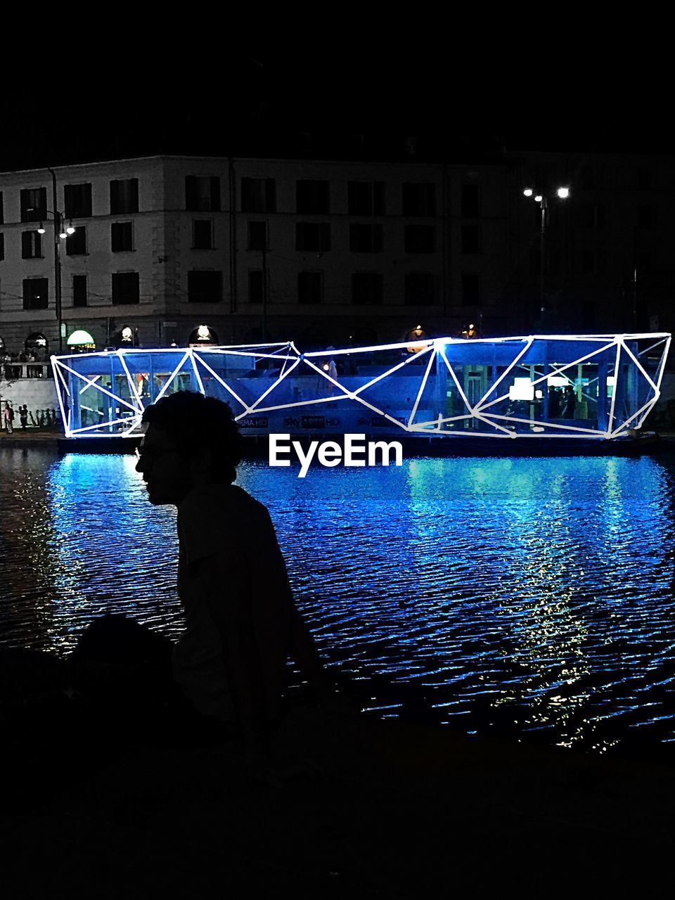 Side view of silhouette man sitting by river at night