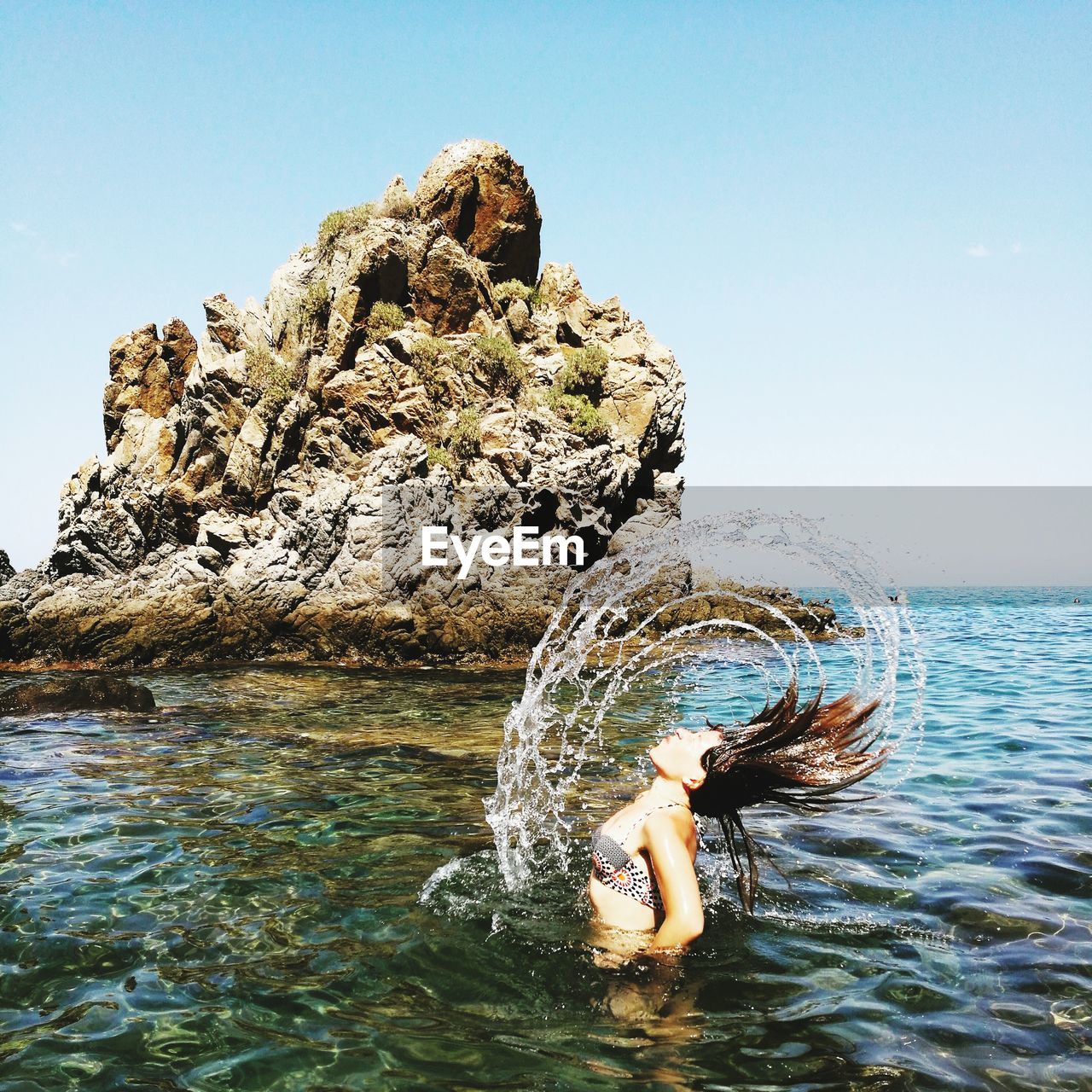 Young woman by rock formation in sea against clear sky