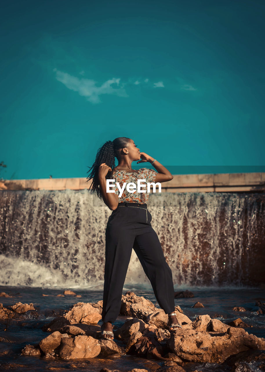 Portrait of young woman standing on rock against dam