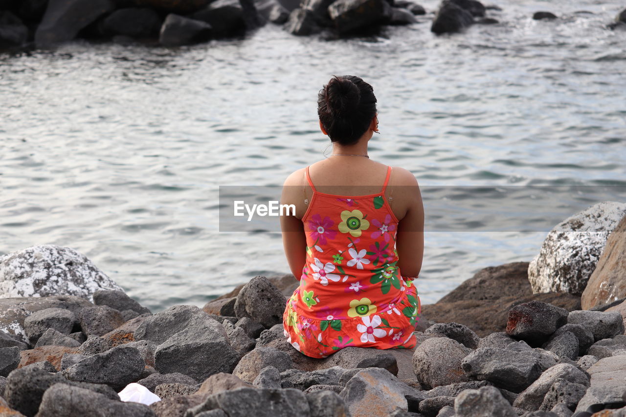 Rear view of woman sitting on rock by sea