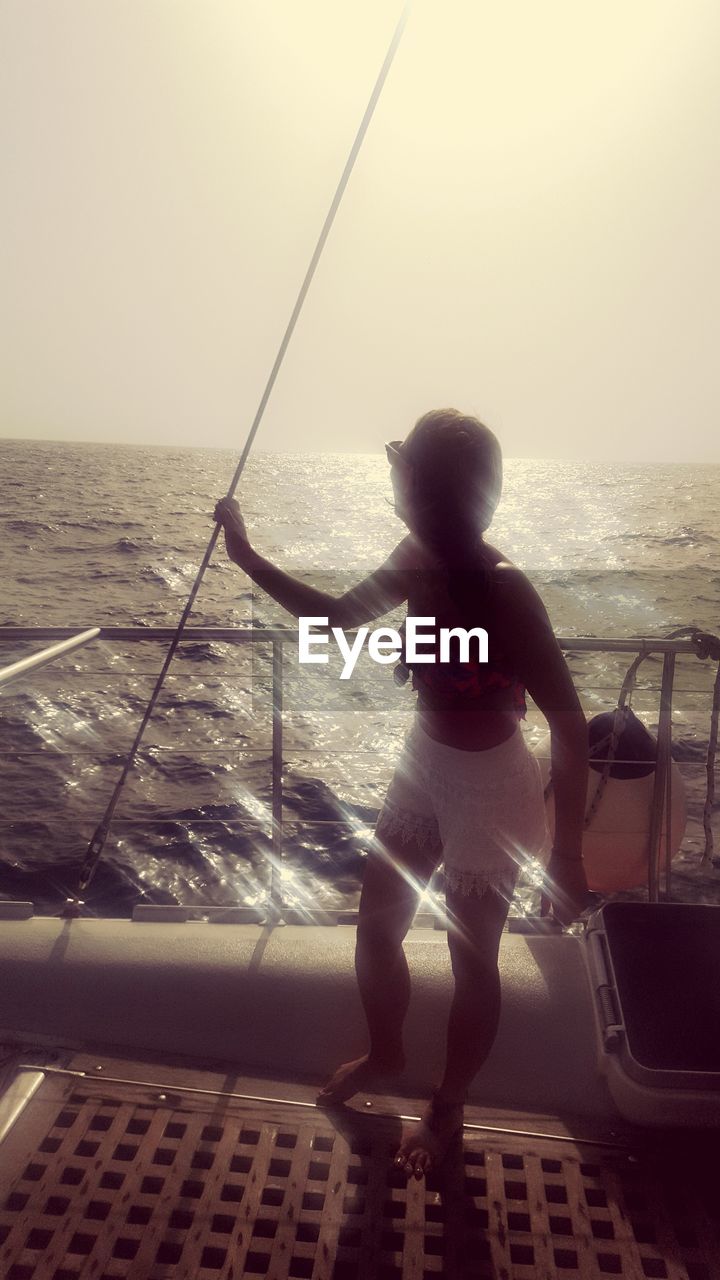 BOY STANDING ON SEA SHORE AGAINST CLEAR SKY