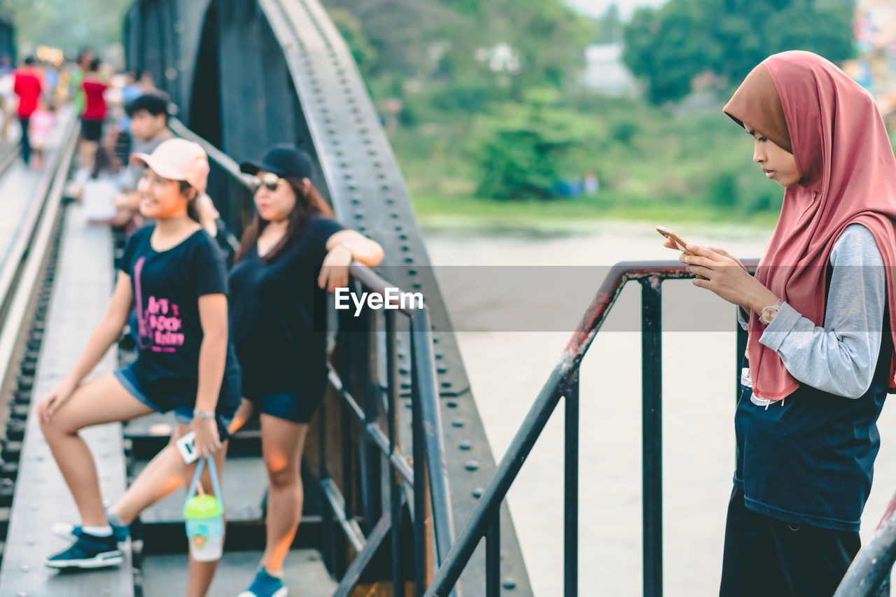 REAR VIEW OF WOMEN STANDING AT RAILING