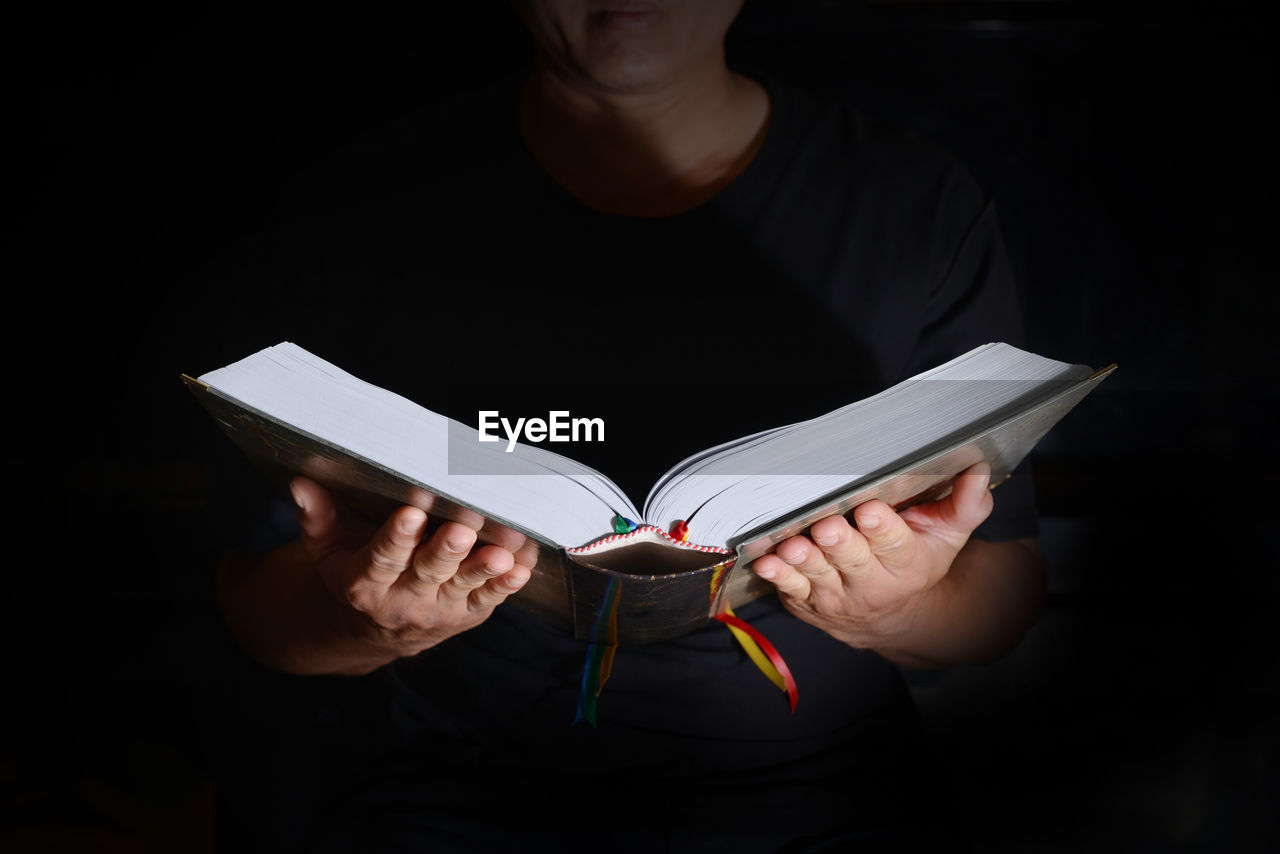 Midsection of woman reading bible in room