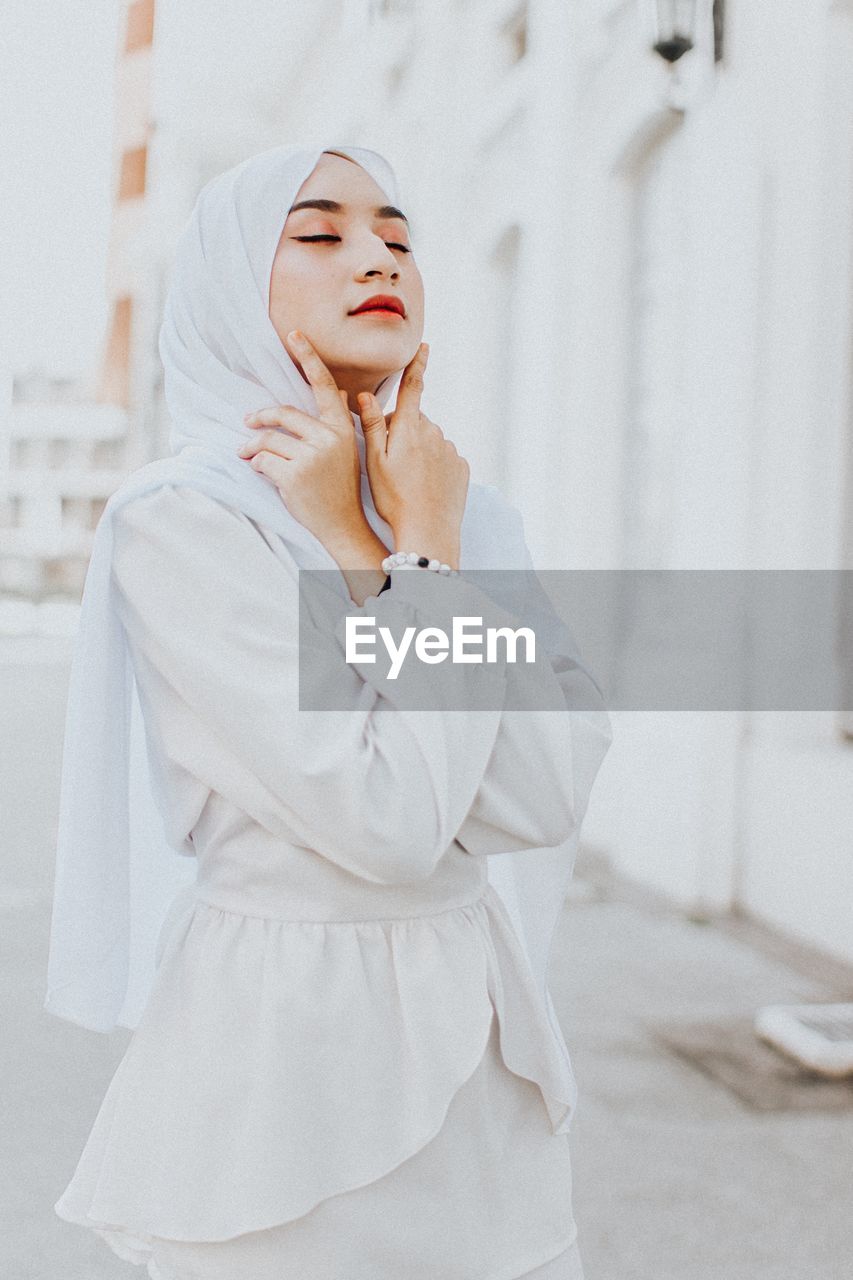 Beautiful young woman wearing hijab while standing against building