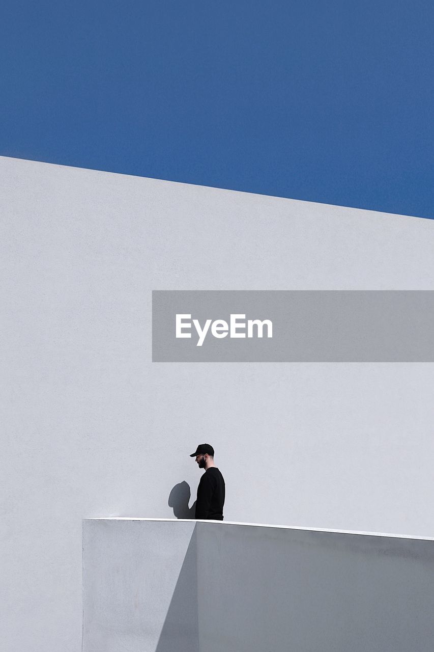 Low angle view of man standing by white wall during sunny day